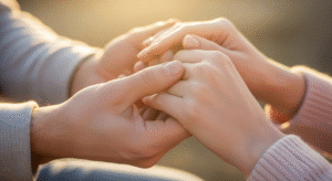 A close-up photo of four hands of a couple gently touching in warm afternoon sunlight, showing tenderness and emotional connection.